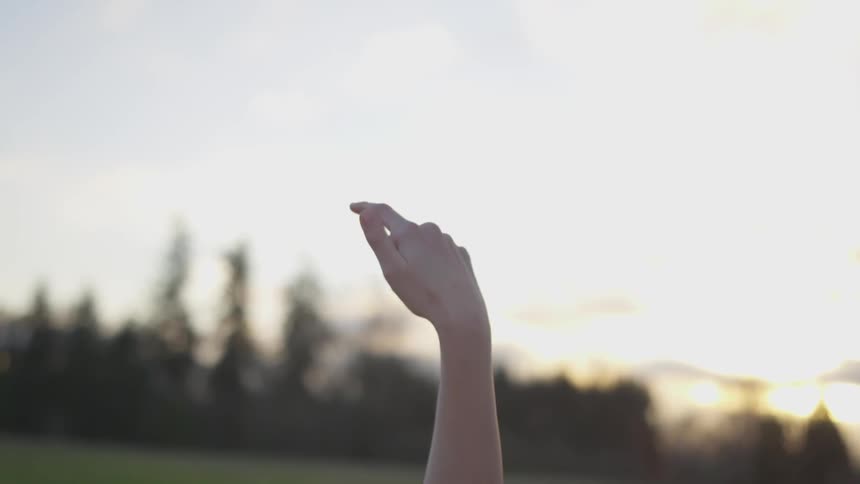 A person points to the sky with one finger as the sun sets