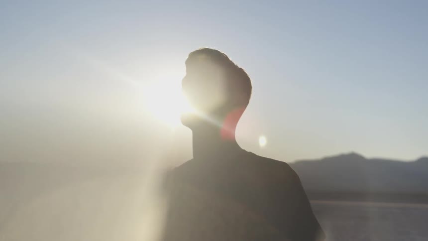 Man stands by a lake with the sun shining down