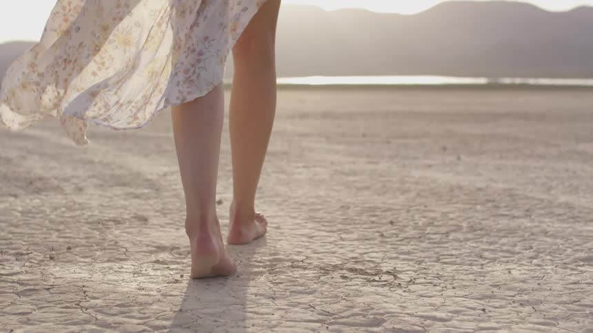A woman in a dress walks along the dry dirt ground