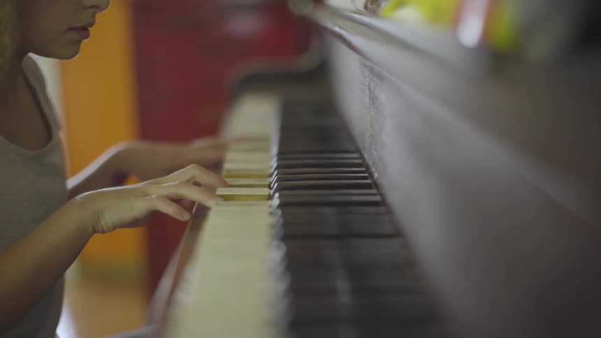 A little girl with blond brown hair sits in front of a piano attempting to play some notes inside