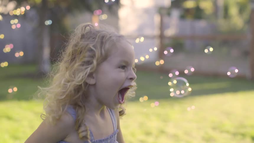 Young girl runs around a yard through bubbles