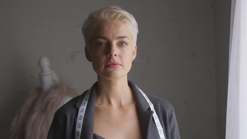 A fashion designer stands with a measuring tape around her shoulders