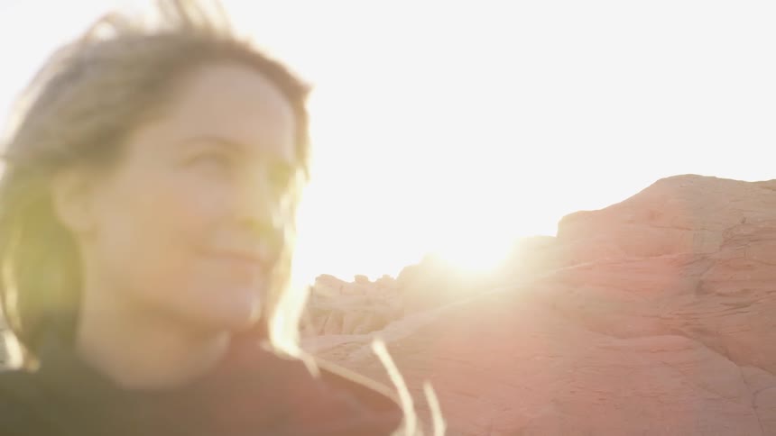 A woman smiles by a mountain on a windy day