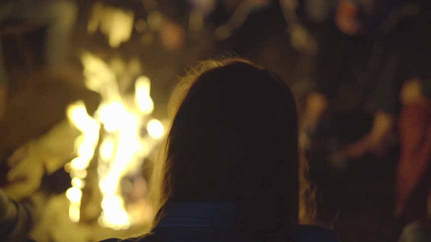 Friends are gathered around a campfire at night