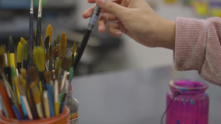 A child grabs a paint brush from a jar