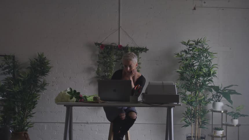 Woman seated at a table reads her laptop
