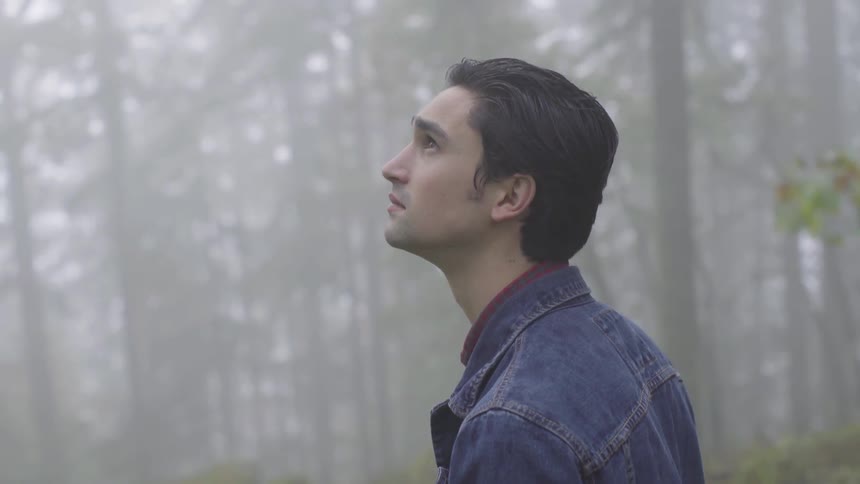 Man stands in foggy forest looking up toward the sky