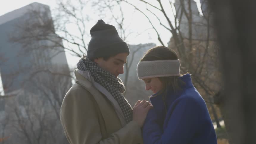 Man holds woman's hand in city on a cold sunny winter day