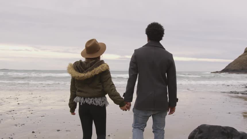 Woman and man walking holding hands on a beach