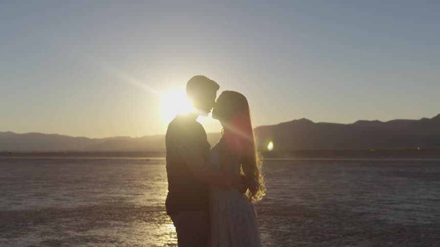 Man and woman holding each other and kissing under the sun