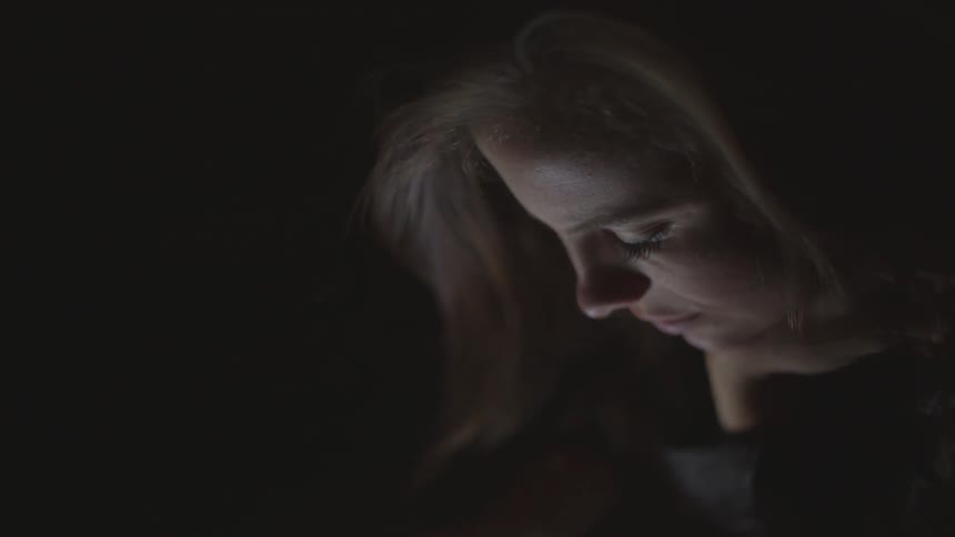 A woman's face is lit up by a screen in the darkness