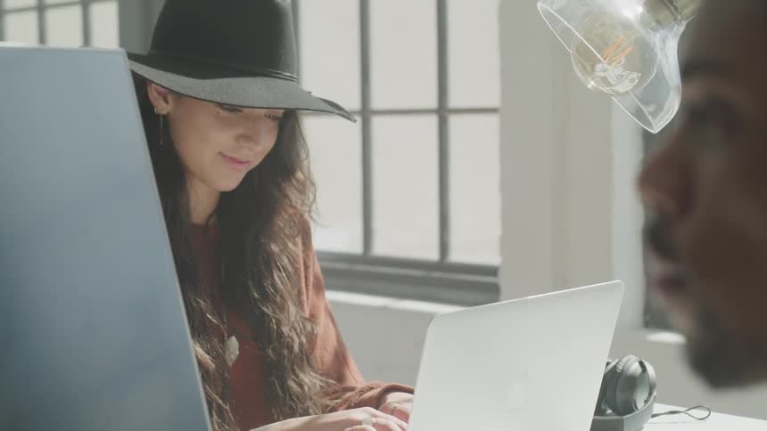 A man and woman sit at a desk and use computers