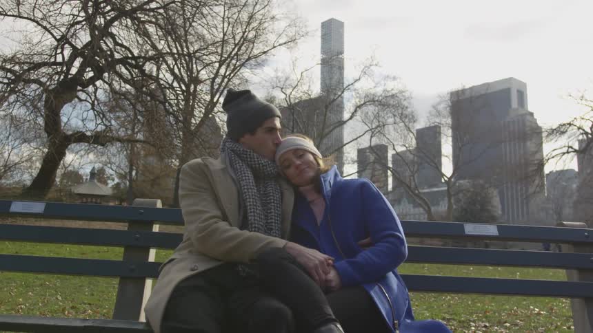 A couple sitting on a bench stays close while holding hands