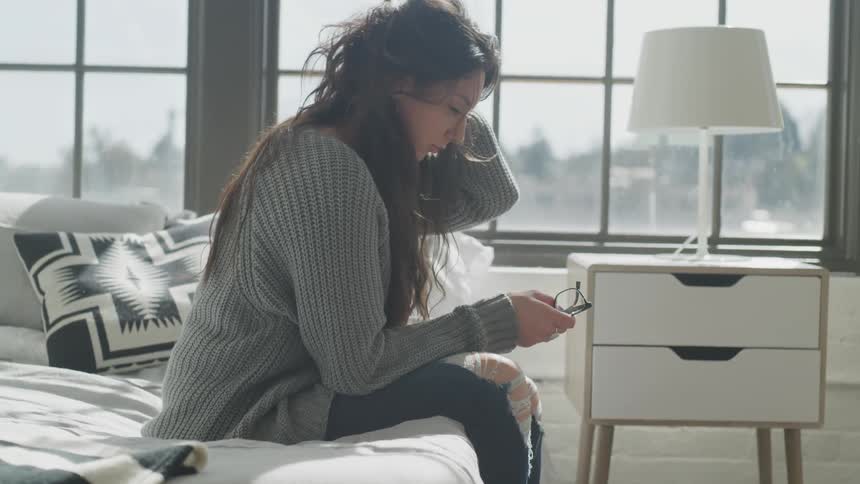 A woman sits on a bed in front of a window