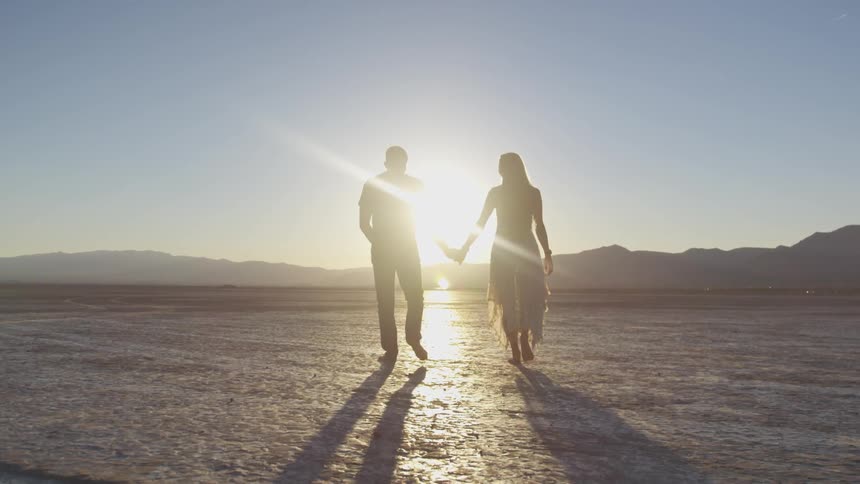 Two people hold hands walking toward the glowing sun