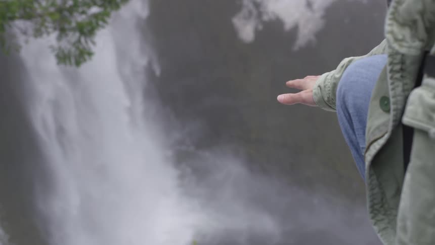 A man reaches towards a waterfall in mountains