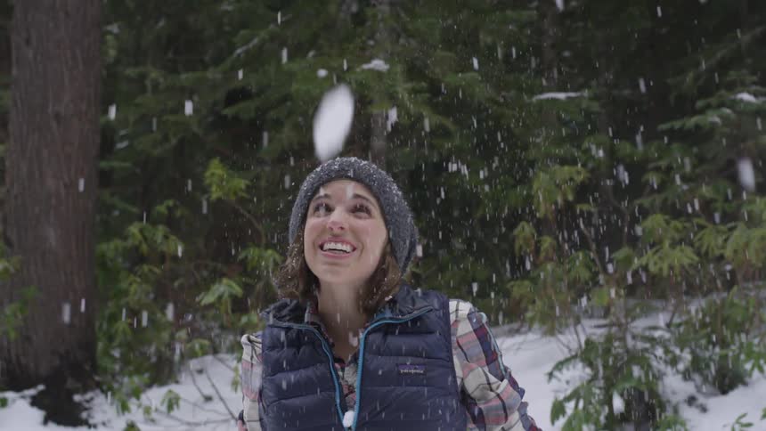 A woman smiles as she throws snow in the air