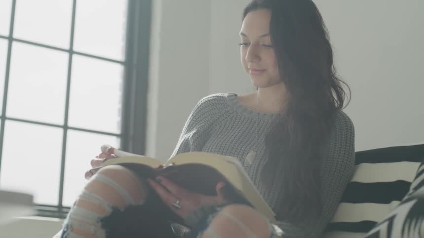Woman with ripped jeans reading a large book in a bright room