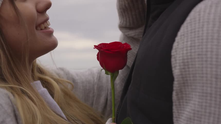 A man and woman embrace lovingly as she holds a red rose