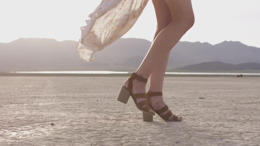 Woman in heels and flowing skirt walks across desert in sunlight