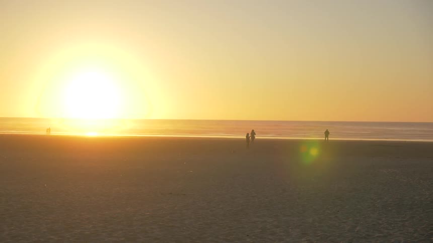 Four people at the beach seen off in the distances as a sunset occurs over the ocean
