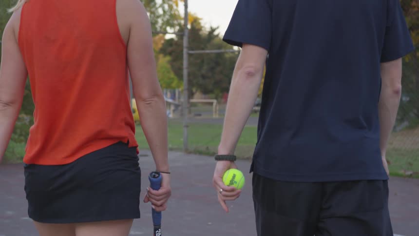 Man and woman walking across a tennis court with rackets and balls