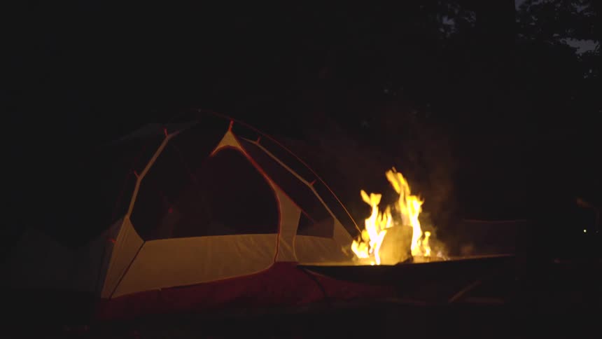 Campfire burns in front of tent at night