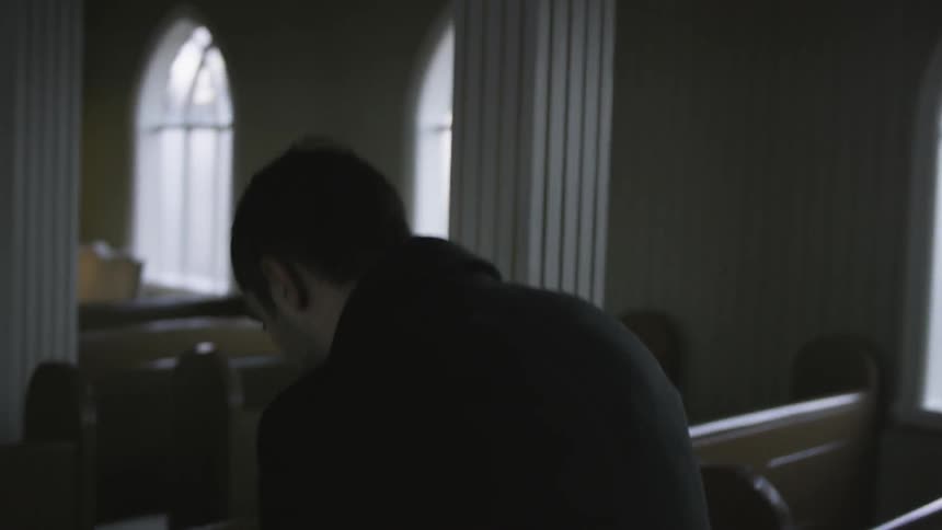 Man walks down the aisle in an empty church and sits in a pew