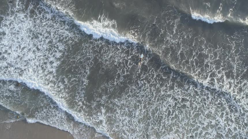 Birds eye view of surfer paddling across crashing ocean waves