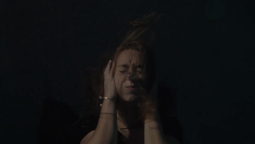 A woman is beneath the water shaking her head before making her way to surface