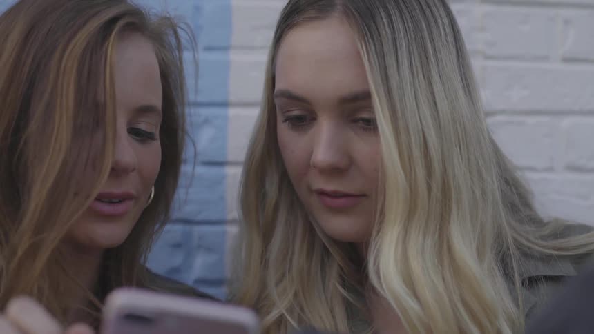 Two women look at a phone and laugh