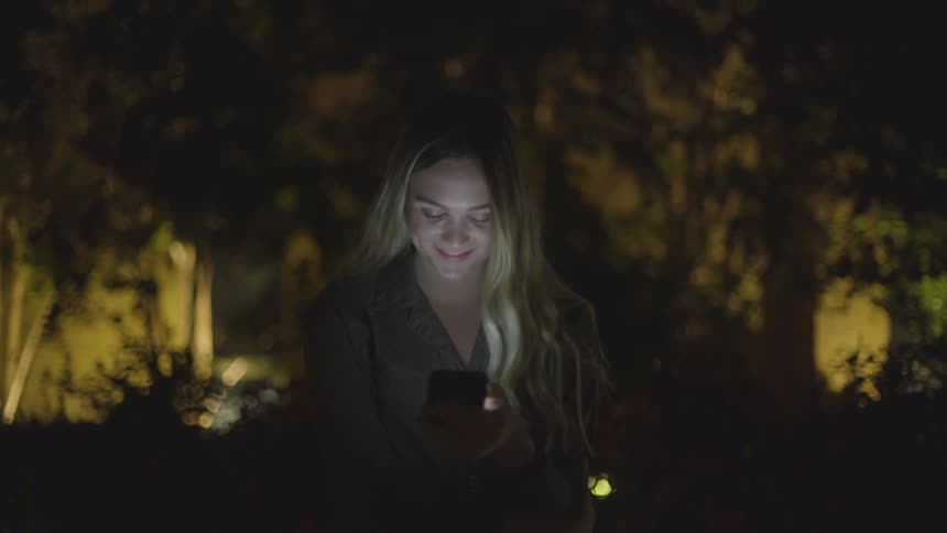 A woman looks down at her phone near a tree
