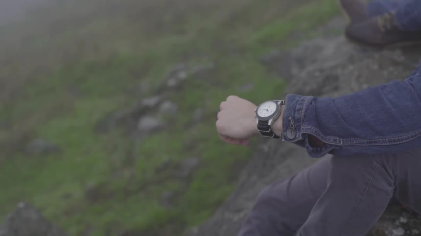 Arm wearing watch with rocky hill in background