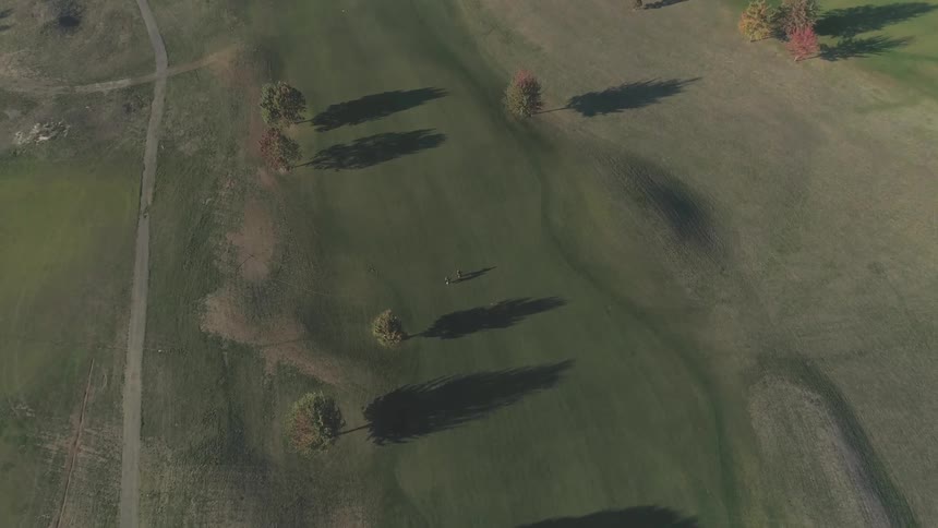 Two people crossing a field with few trees