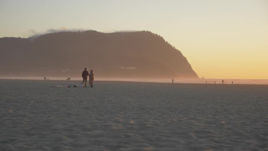 Two people walk across a beach side by side at sunset