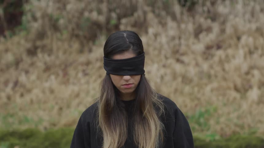 A woman wears a black blindfold over her eyes as she kneels