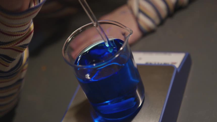 A girl stirs a blue liquid during a science experiment