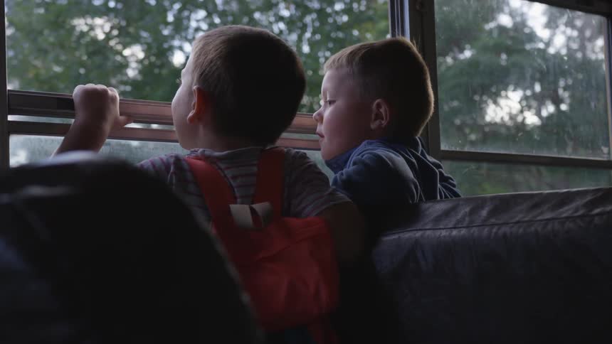 Two kids looks out of a bus window as it passes trees