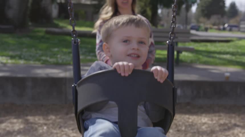 A woman pushes a young child on the swing
