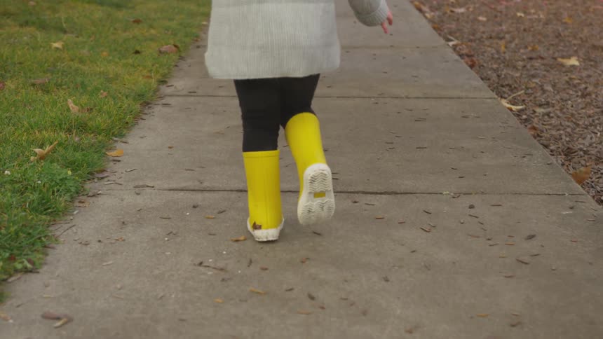 Young child running down the sidewalk in yellow rain books