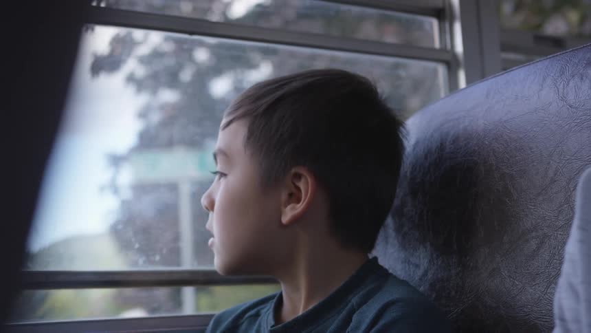 A small child looks out the window of a school bus