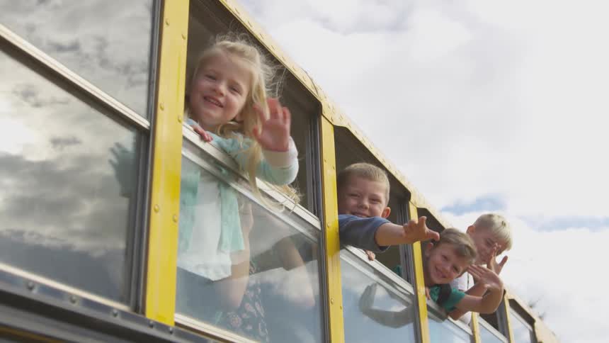 Boys and girls waving from the windows of a school bus