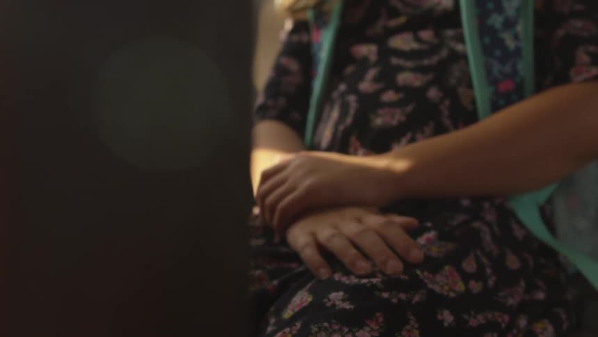 A girl in a dress sits with her hands folded
