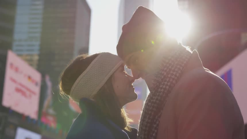 A man and woman touch noses and smile at each other in the middle of the city