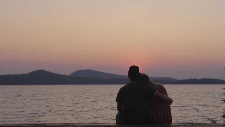 A man has his arm around a woman sitting by the water