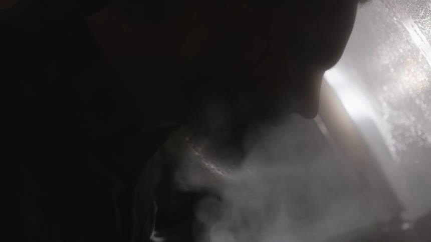Man sits in darkness with steam floating to his face