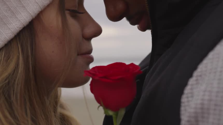 A young couple embrace one another as rolling waves meet the beach on which they stand