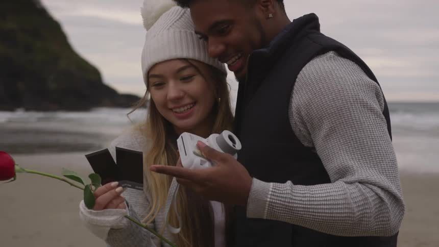 Woman and man look at pictures on beach and laugh