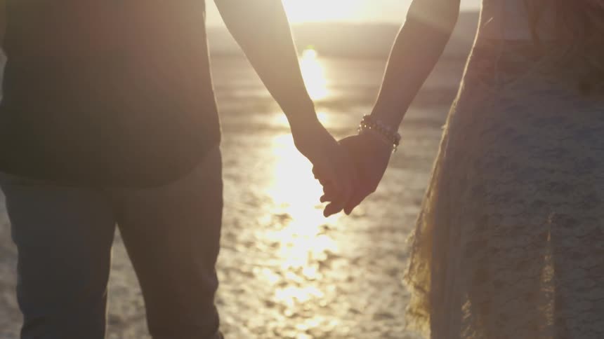 Man and woman holding hands and walking into the sunset