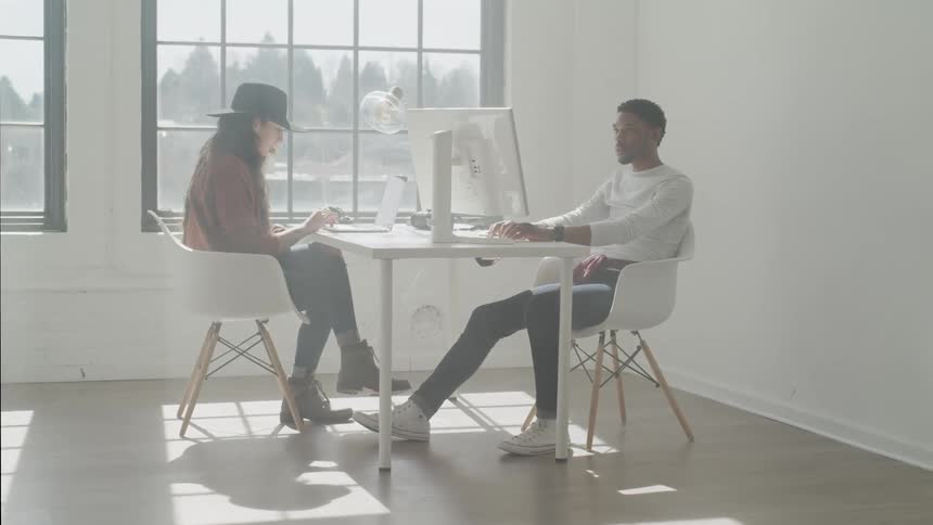 Man and woman sit at a white table as they work on their computers
